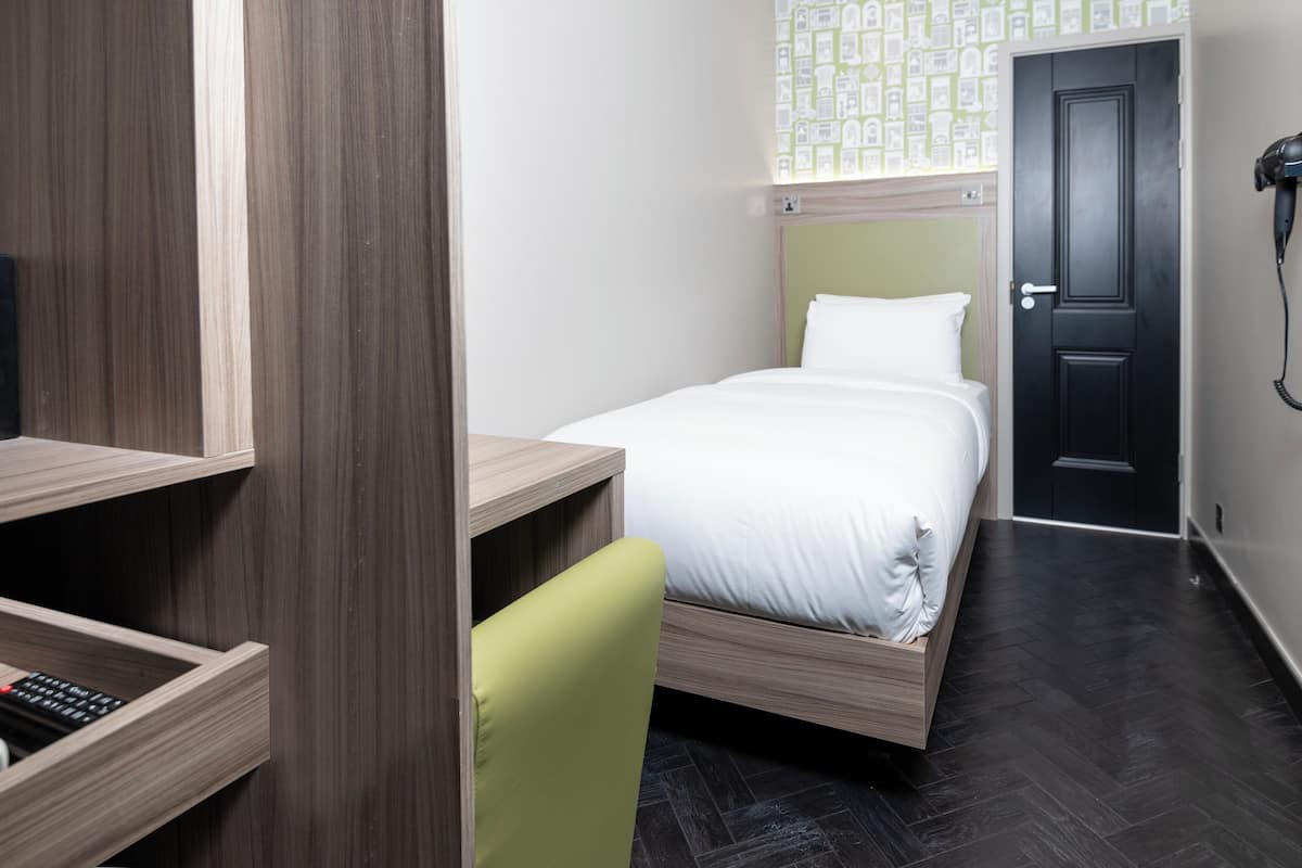 A compact hotel room with a bed, a desk, a chair, and a wardrobe.