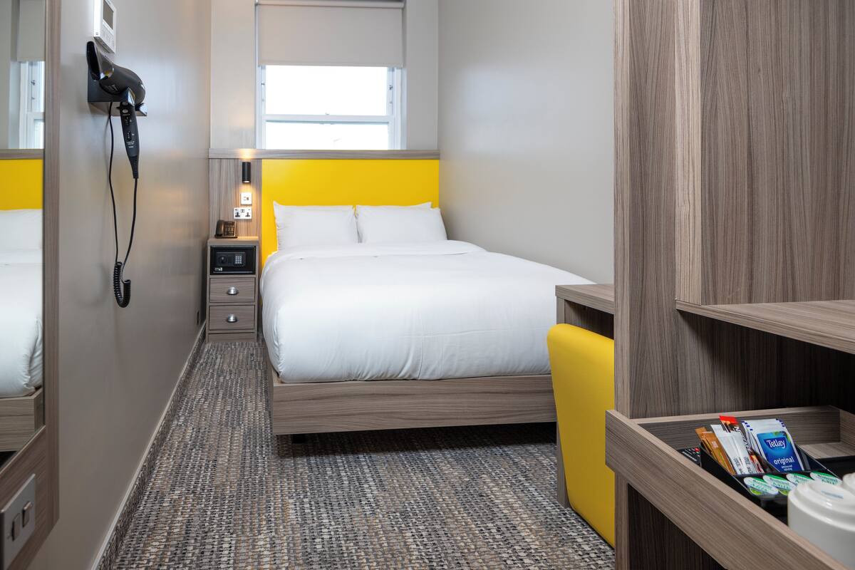 A hotel room with a bed, a bedside table, a hairdryer, a nightstand, and a window.