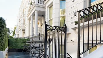 Una entrada de hotel con una reja de hierro forjado negro, una escalera y una fila de sillas afuera.