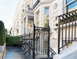 Ein Hotel Eingang mit einem schwarzen schmiedeeisernen Tor, einer Treppe und einer Reihe von Stühlen davor.