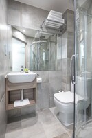 Un baño moderno con cabina de ducha de vidrio, un lavabo blanco y un inodoro.