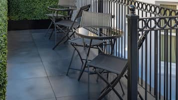 A terrace with a black metal fence, a table with chairs, and a row of windows with white columns.