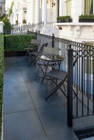 A terrace with a black metal fence, a table with chairs, and a row of windows with white columns.