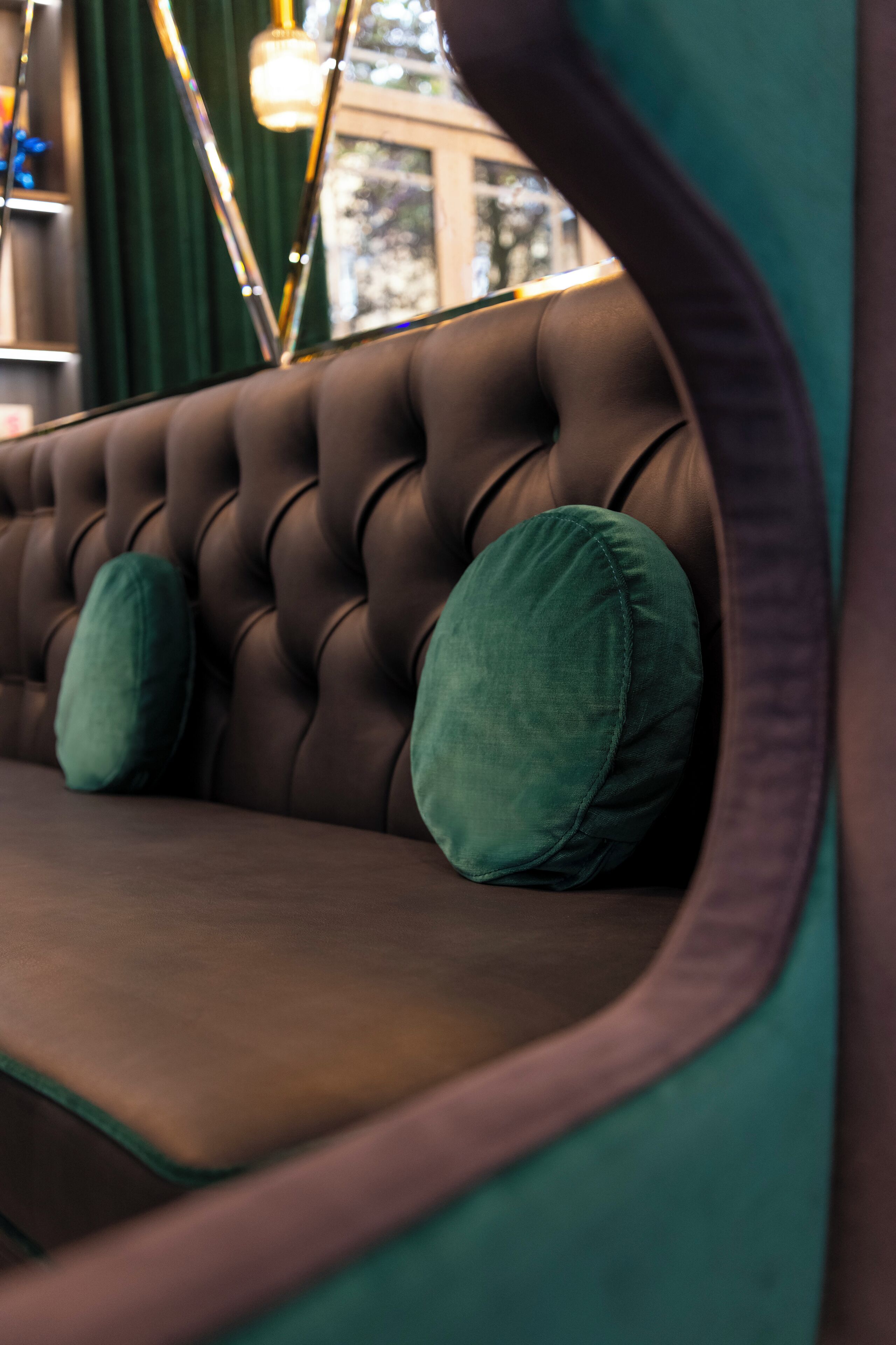 A tufted brown sofa with green cushions in a room with teal walls and a window.