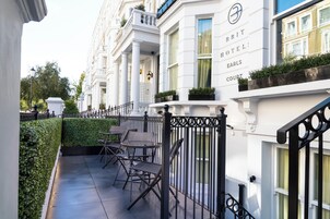 Hotelgevel in het wit, met een zwarte ijzeren balustrade en een klein terras met stoelen en tafels.