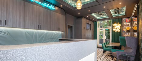 Un espace d'accueil moderne, doté d'une enseigne au néon, d'un comptoir de réception et d'un coin salon avec des chaises vertes et une table.