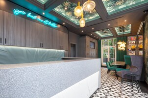 Ein moderner Empfangsbereich mit einer Neonreklame, einem Empfangstresen und einer Sitzecke mit grünen Stühlen und einem Tisch.