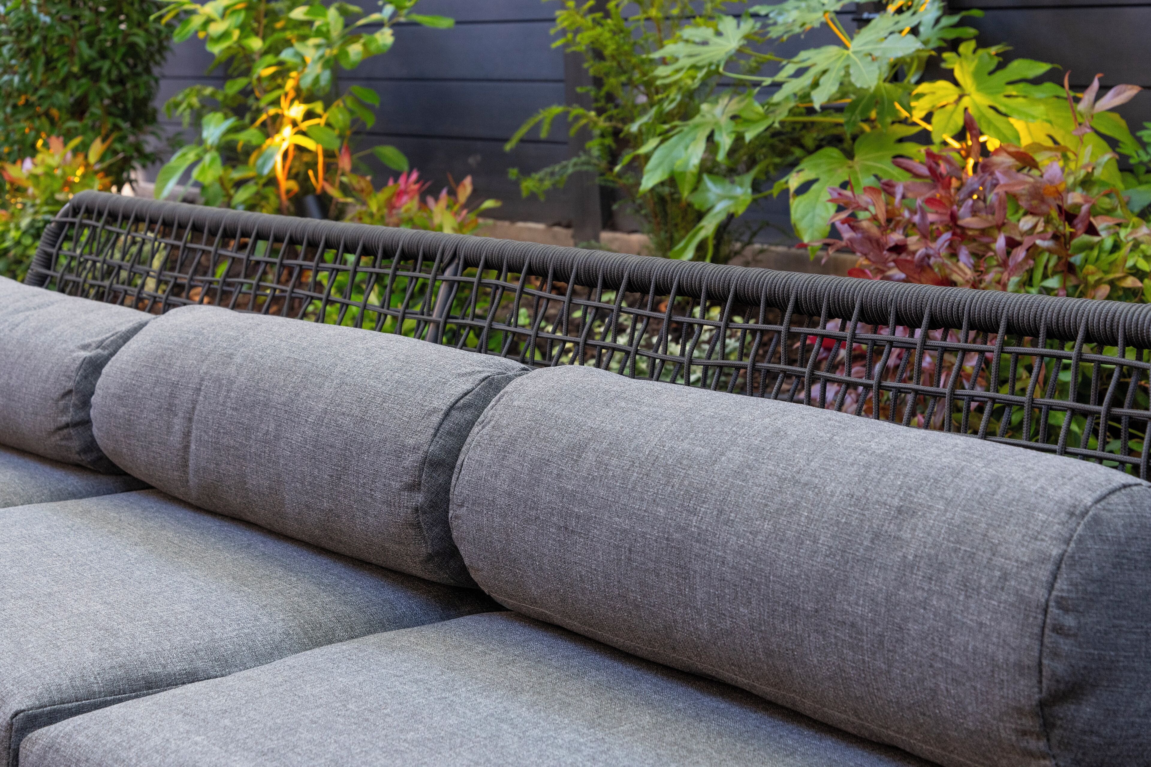 A wicker sofa with grey cushions in an outdoor setting.