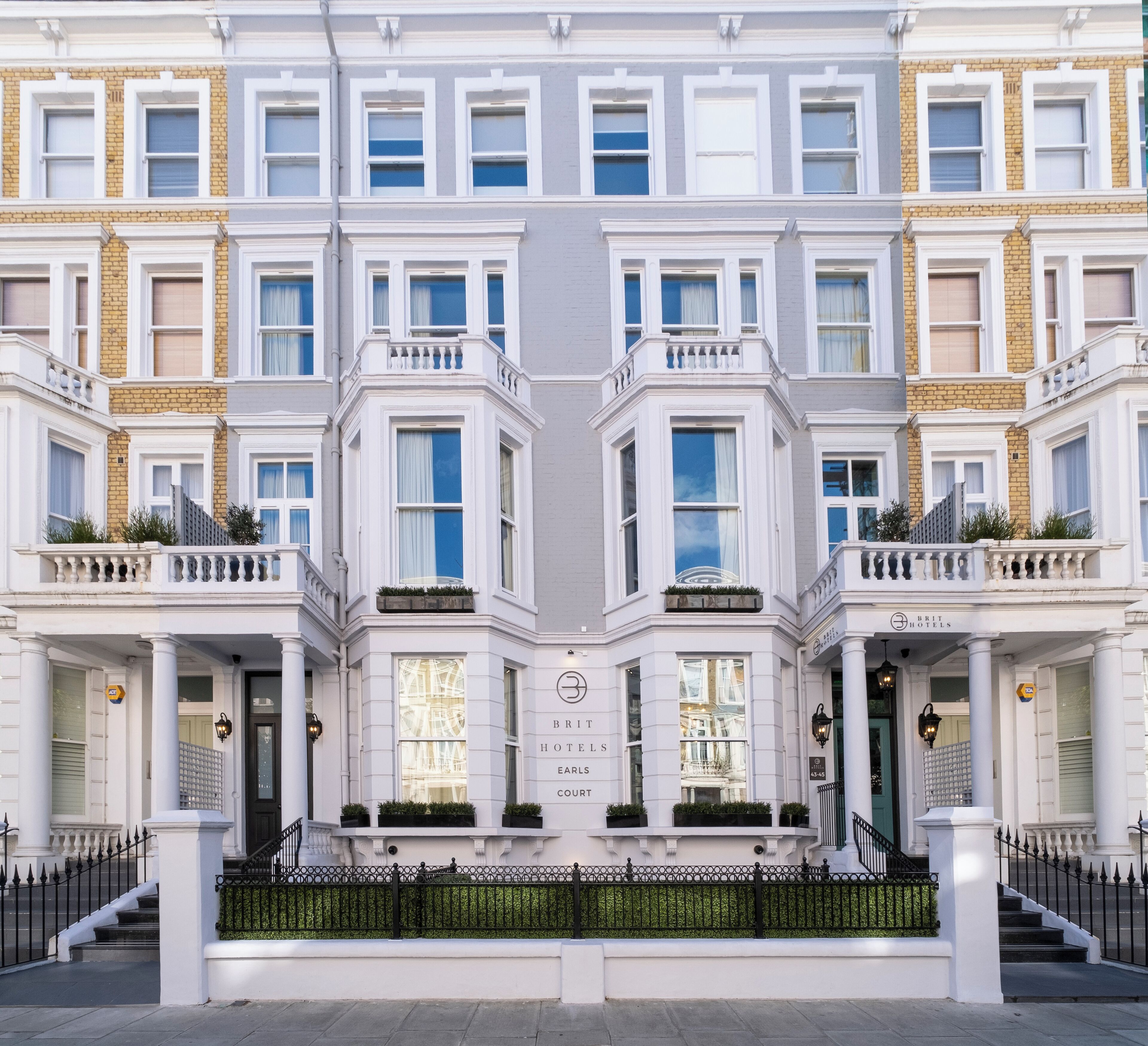 A symmetrical building facade with a central entrance, multiple windows, and a sign for 'Brit Hotels Earls Court'.