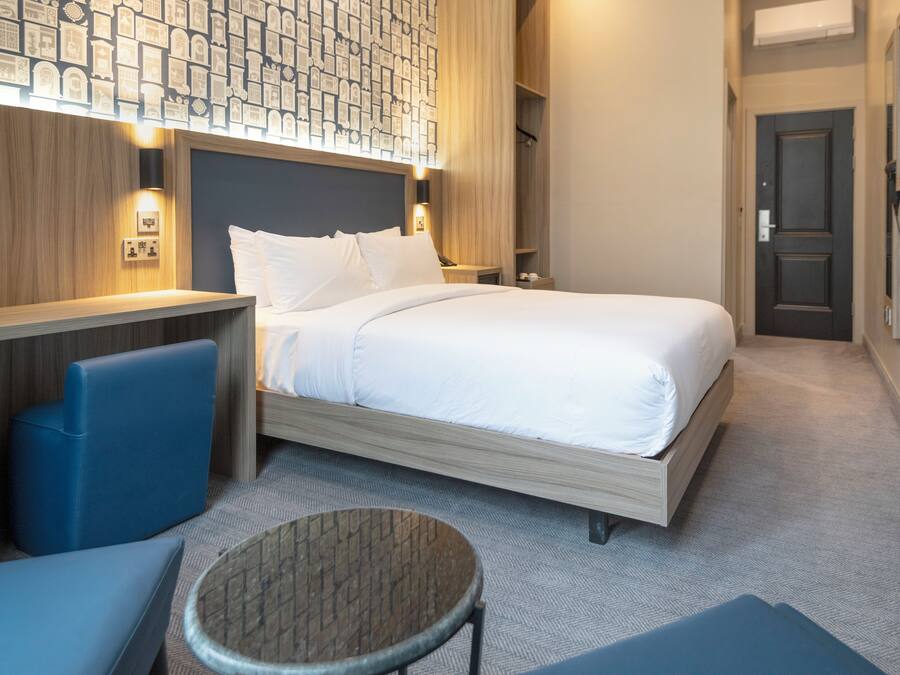 A hotel room with a bed, a seating area with a chair and a small table, and a wall with a patterned design.