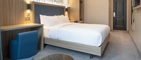 A hotel room with a large bed, a desk, a chair, a small round table, and a wall with a patterned design.