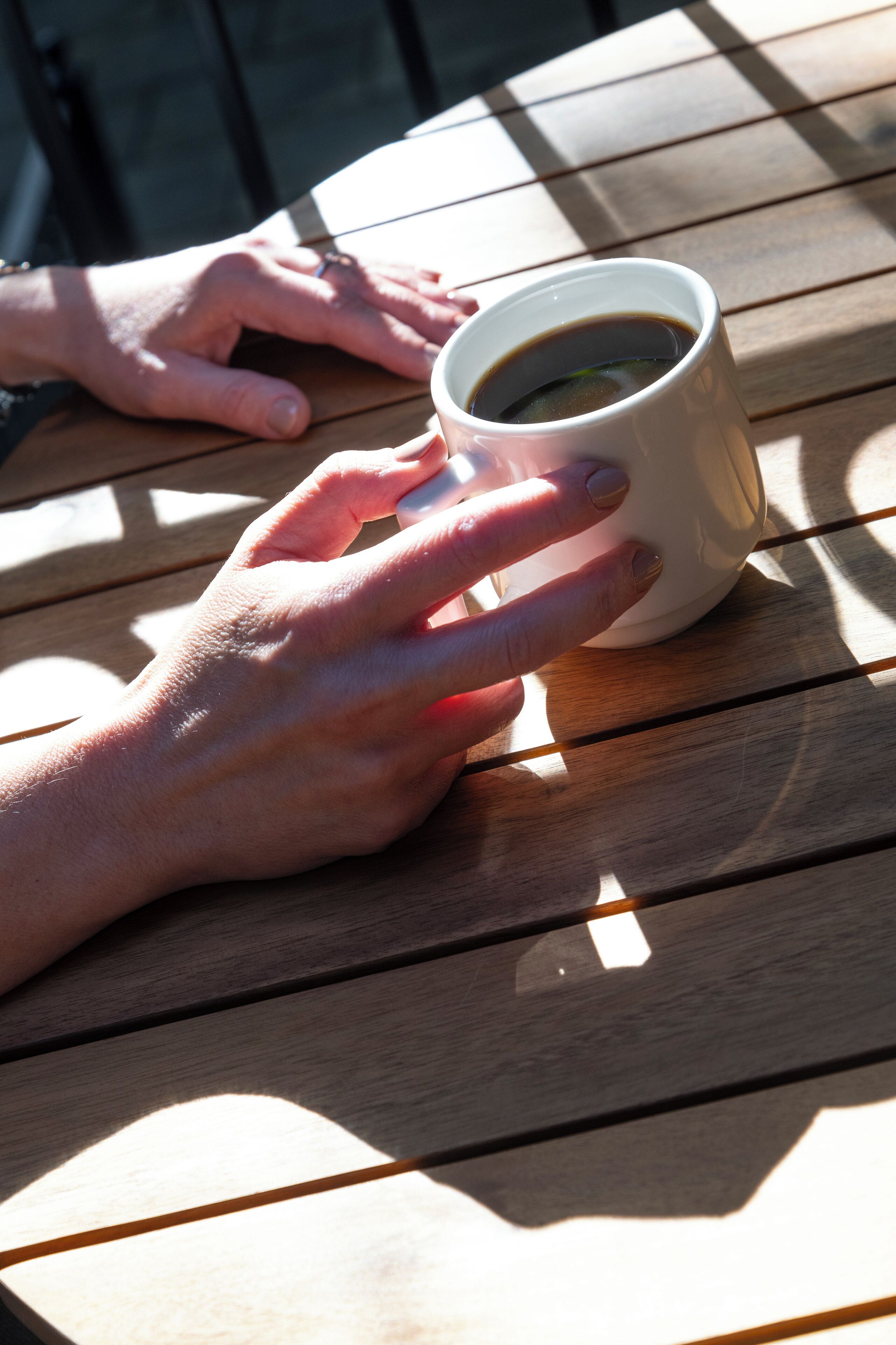 A hand holding a cup of coffee on a wooden table.