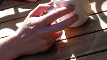 A hand holding a cup of coffee on a wooden table.