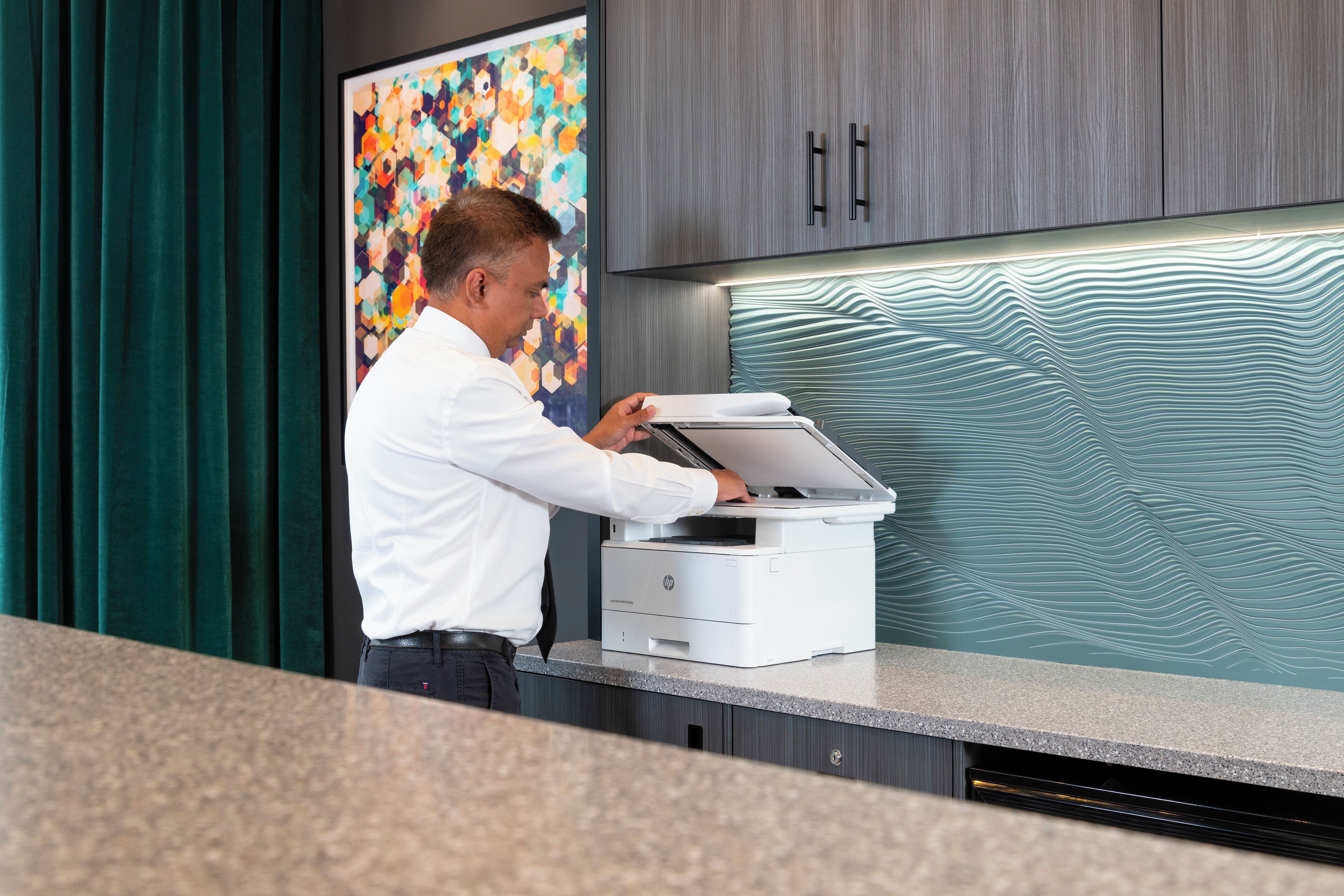A person operating a printer in a modern office setting with a colorful abstract painting and sleek cabinetry.