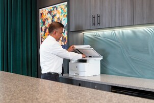 Eine Person bedient einen Drucker in einem modernen Büro mit einem farbenfrohen abstrakten Gemälde und eleganten Schränken.