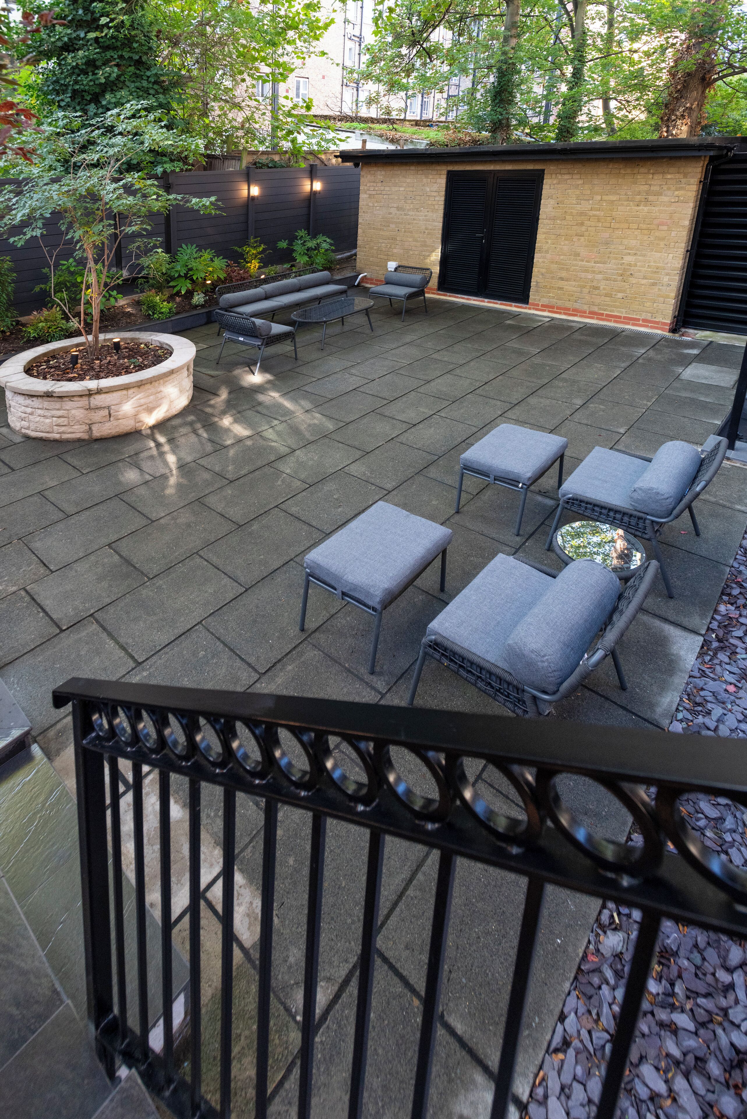 An outdoor patio area with a brick wall, a black metal fence, and a seating arrangement including a table and chairs.