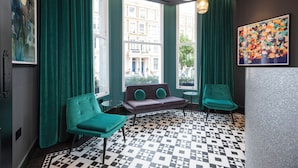 A room with teal curtains, a patterned floor, a sofa with teal cushions, and a painting on the wall. - Brit Hotels Earls Court (London)