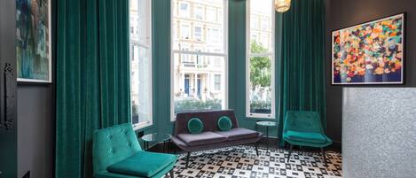 A room with teal curtains, a patterned floor, a sofa with teal cushions, and a painting on the wall.