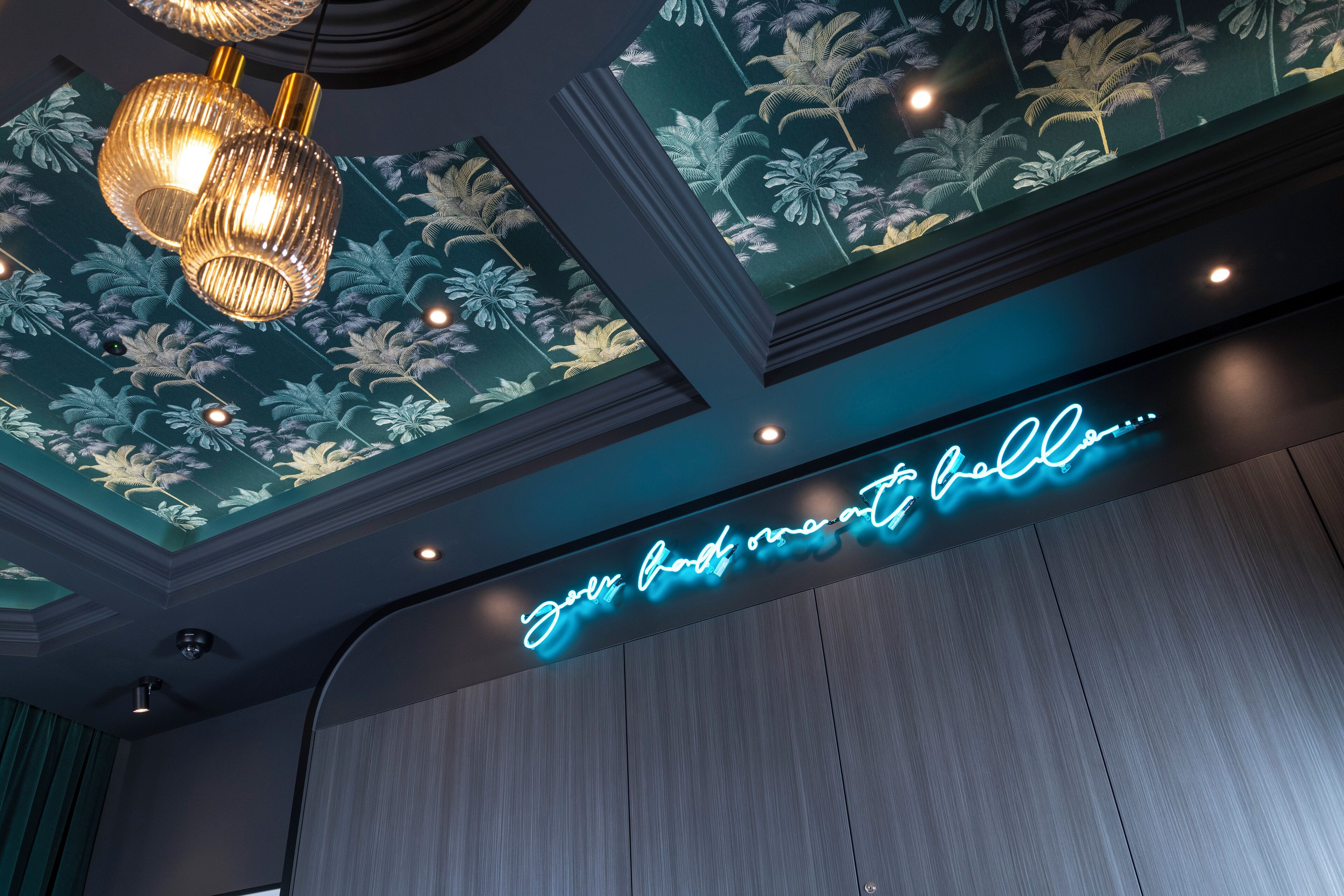 Eine Decke mit floralem Muster und ein Neon-Schild mit der Aufschrift 'Your home to hell'.