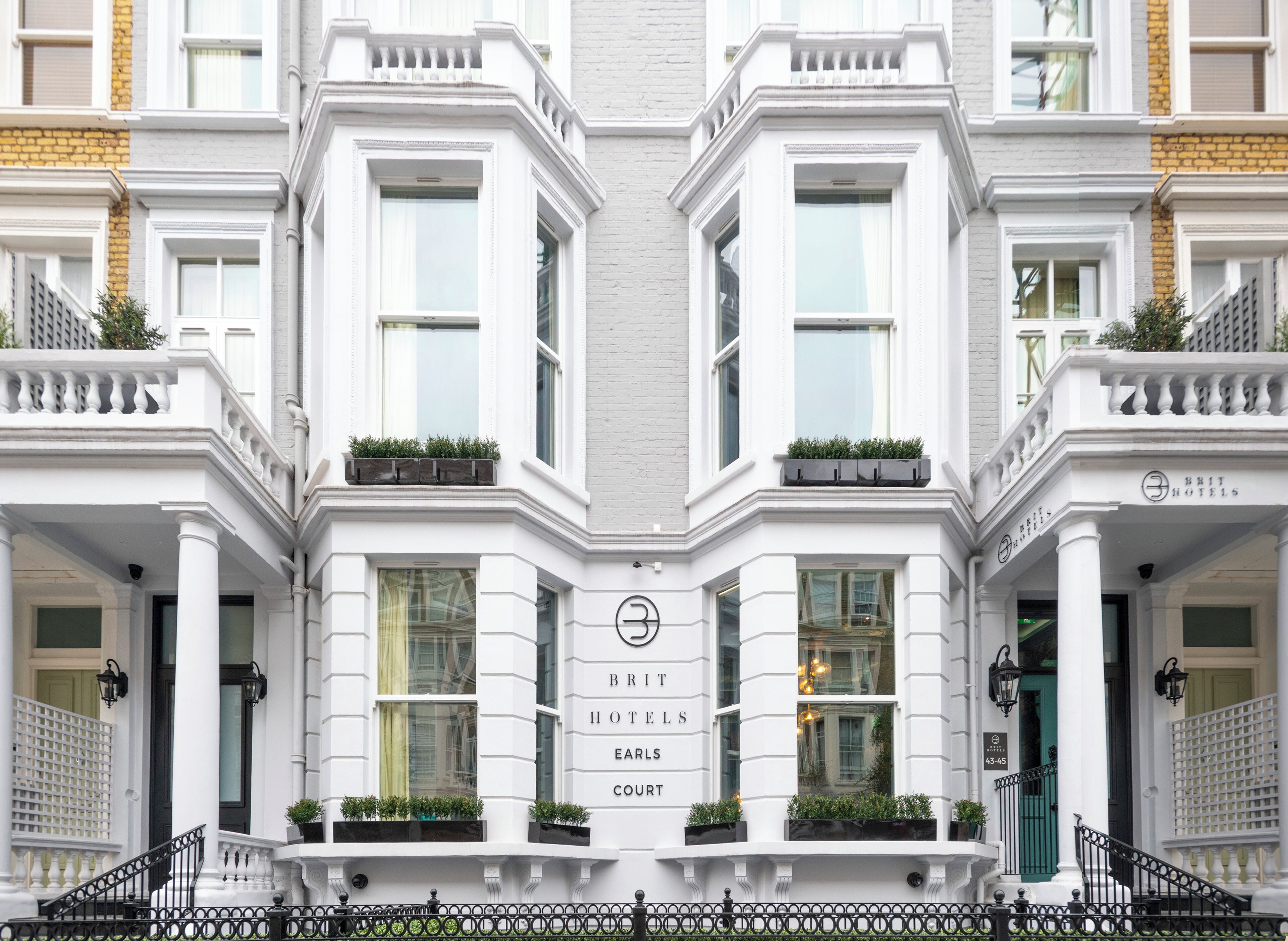 A corner building with a symmetrical facade, large windows, and a central entrance with a sign for 'BRIT HOTELS EARLS COURT.'