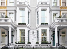 Ein Eckgebäude mit einer symmetrischen Fassade, großen Fenstern und einem zentralen Eingang mit einem Schild für 'BRIT HOTELS EARLS COURT'.