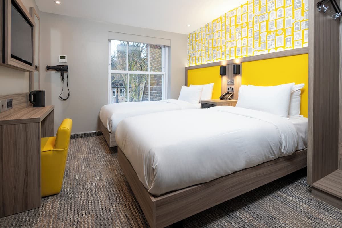 A hotel room with a large bed, a desk, a chair, and a window with a view of buildings.