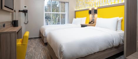 A hotel room with a large bed, a desk, a chair, and a window with a view of buildings.
