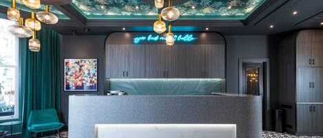 Un espace d’accueil moderne avec un comptoir en marbre, des rideaux turquoise et une fresque murale au plafond.
