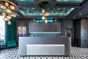 Una zona de recepción moderna con mostrador de mármol, cortinas color turquesa y un mural en el techo.
