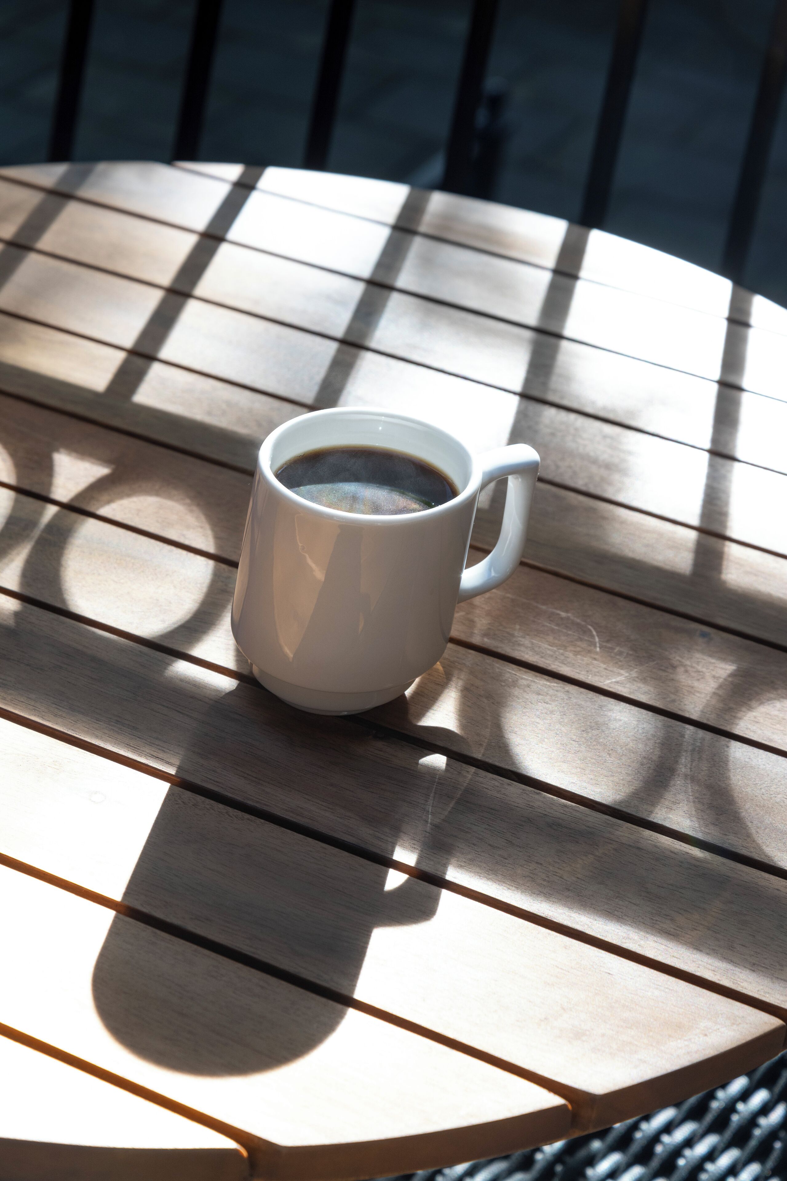 Een witte koffiekop op een houten tafel, met een schaduw.