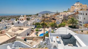 Un pueblo costero con edificios blancos, una piscina azul y vistas al mar y una montaña en la distancia.