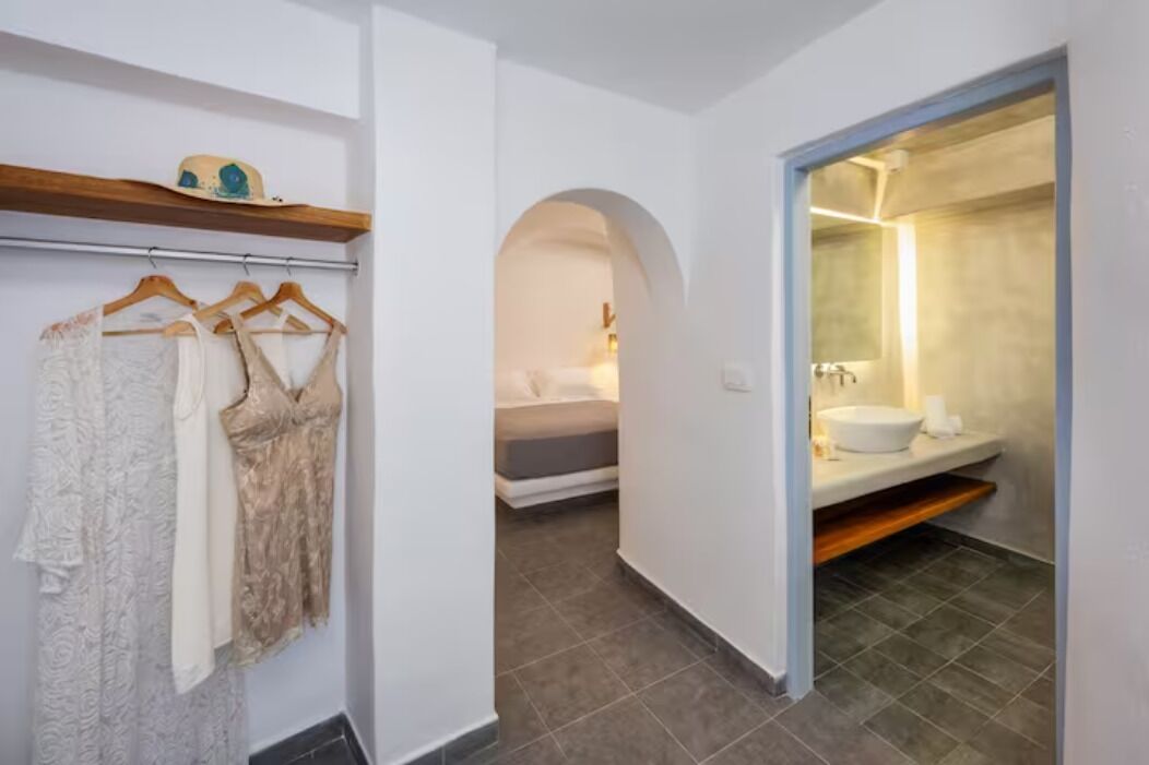 A hallway with a clothing rack, a bed, and a bathroom with a sink and mirror.