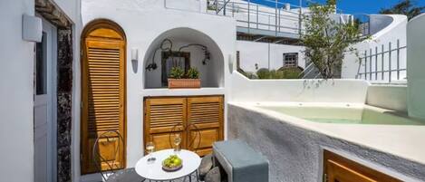 A compact outdoor seating area with a table and chairs, a wooden door, and a small garden.
