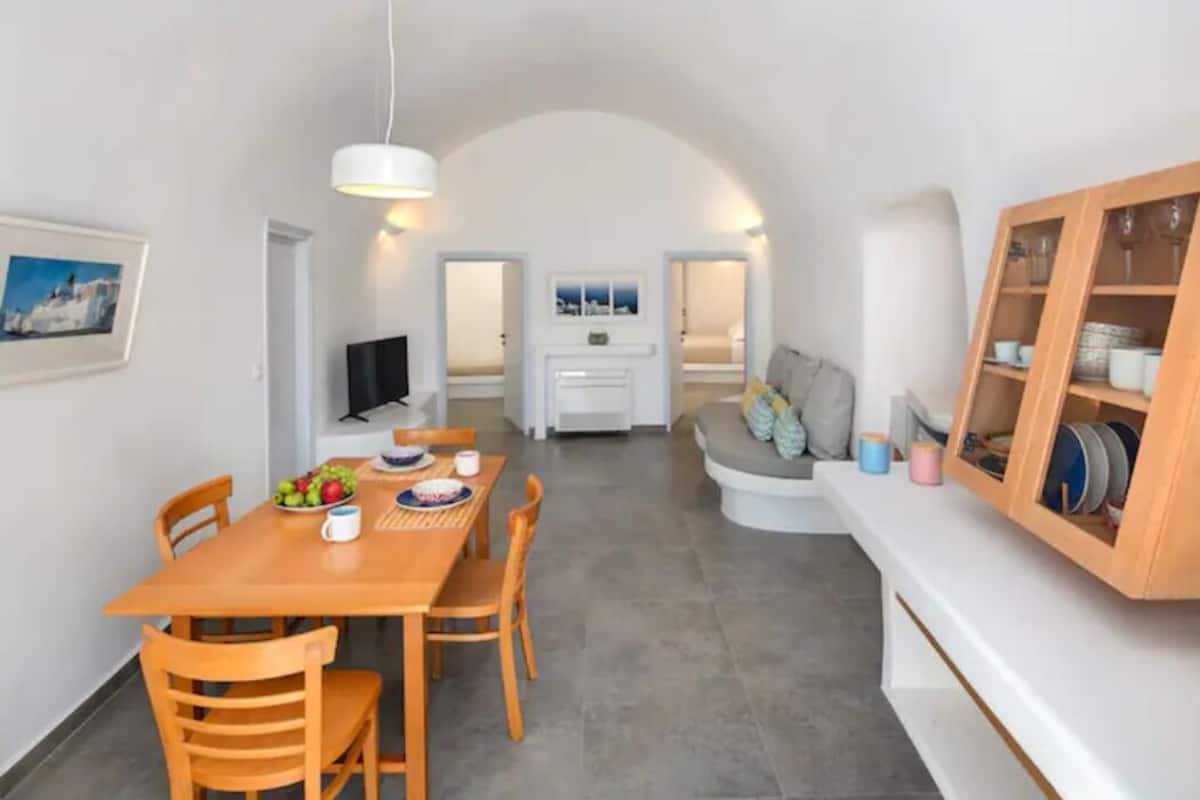 A modern kitchen with a dining area, white walls, and a cozy seating area with cushions.