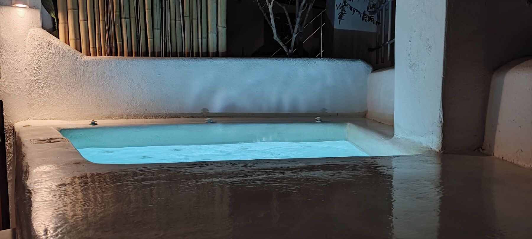 A rectangular bathtub with a smooth, reflective surface, surrounded by a textured wall and a bamboo backdrop.