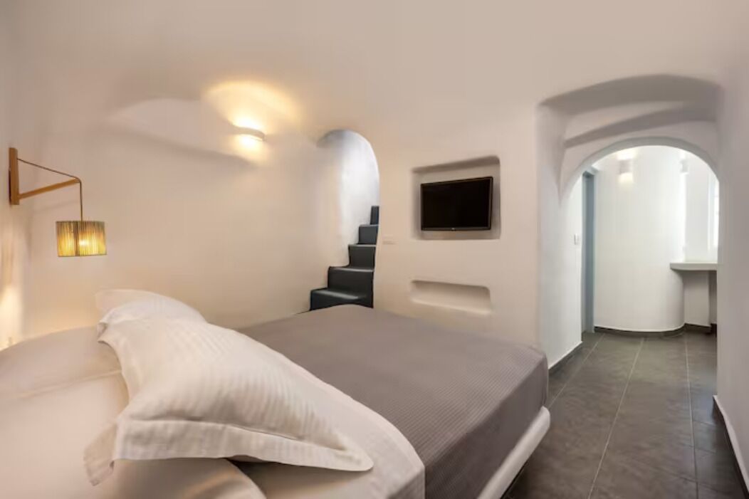 A modern bedroom with a large bed, a TV mounted on the wall, and a staircase leading to another room.