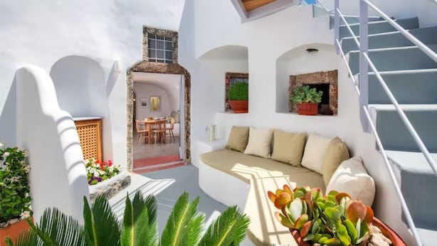 Una habitación moderna de paredes blancas con un sofá, una escalera y plantas en macetas.