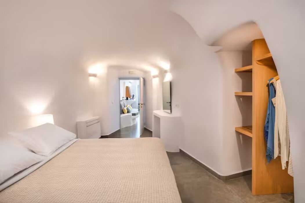 A bedroom with a bed, a wooden wardrobe, and a bathroom visible in the background.