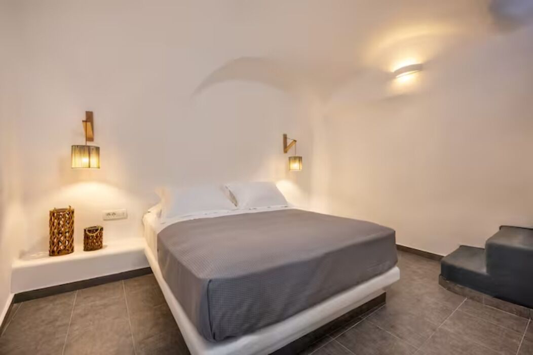 Une chambre d’hôtel moderne avec un grand lit, deux lampes fixées au mur et un petit banc.