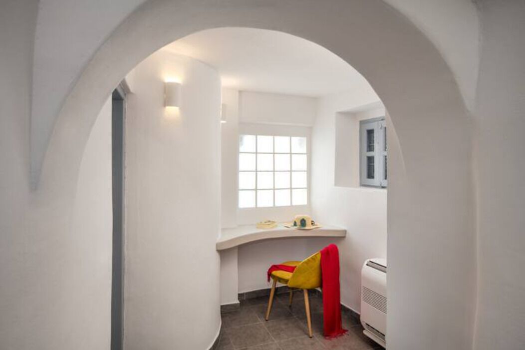 A narrow room with a curved white wall, a window, a chair, and a radiator.