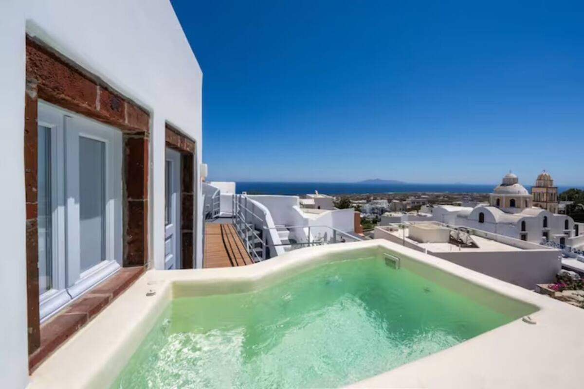 A rooftop pool with a clear view of the sea and white buildings in the background.