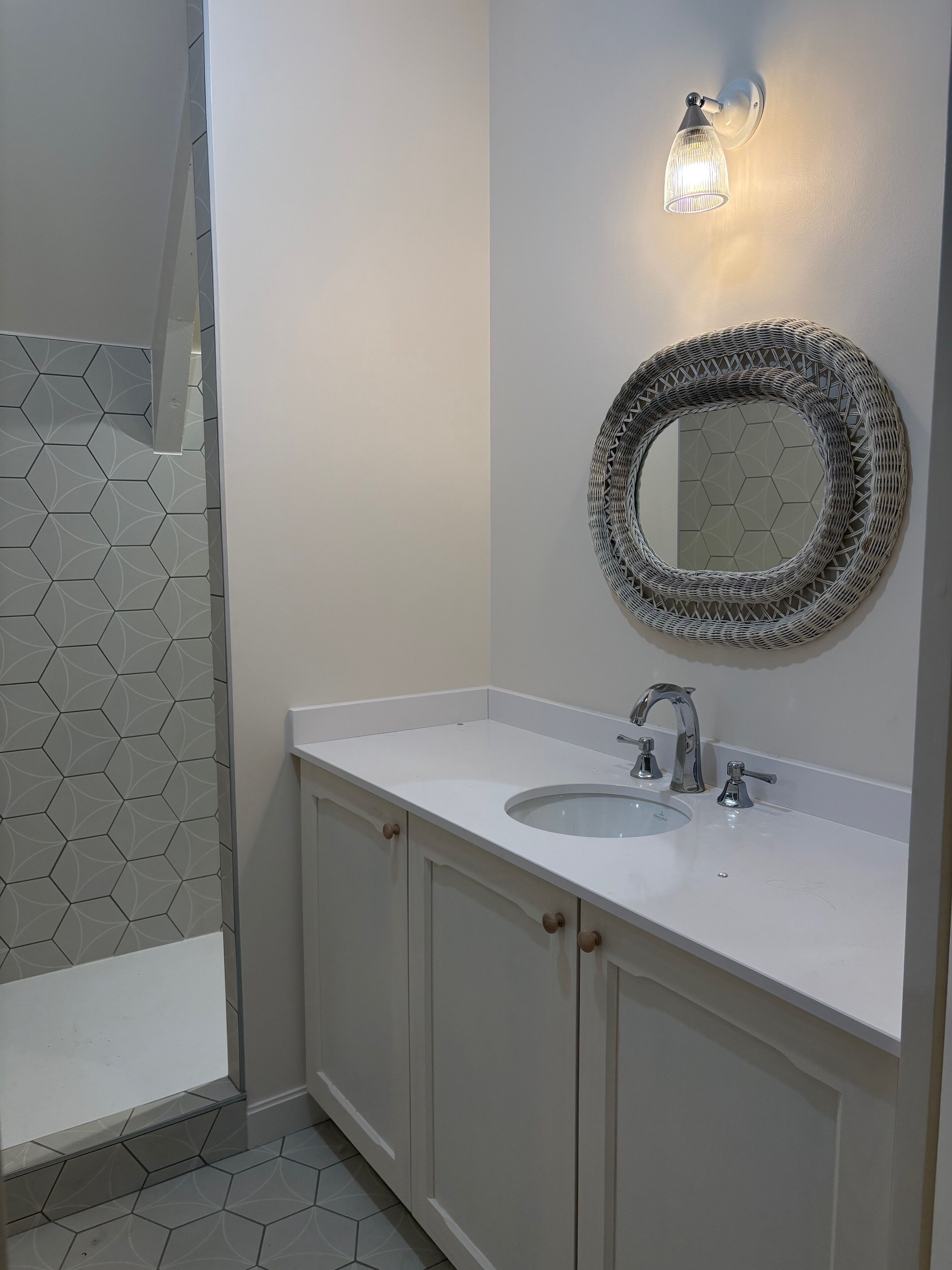 A bathroom with a white sink, a round mirror, and a hexagonal patterned shower area.