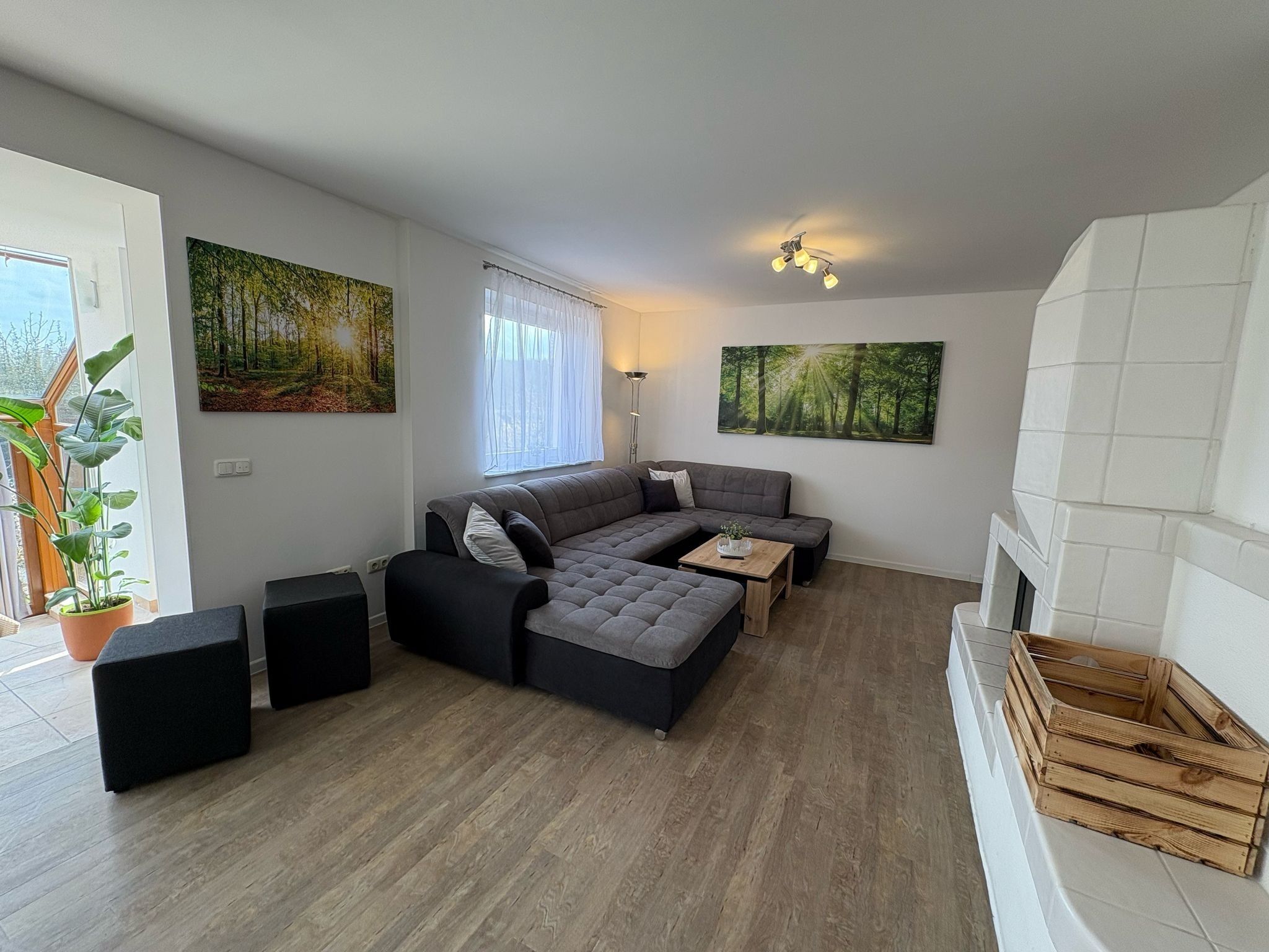 Uma sala de estar moderna com um sofá seccional, uma lareira e duas grandes pinturas com tema de floresta.