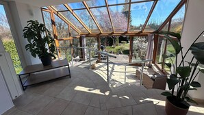 Een ruim balkon met glazen omheining, potplanten en uitzicht op de tuin.