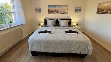 Een slaapkamer met een bed, twee nachtkastjes, een raam met gordijnen en drie foto's aan de muur.