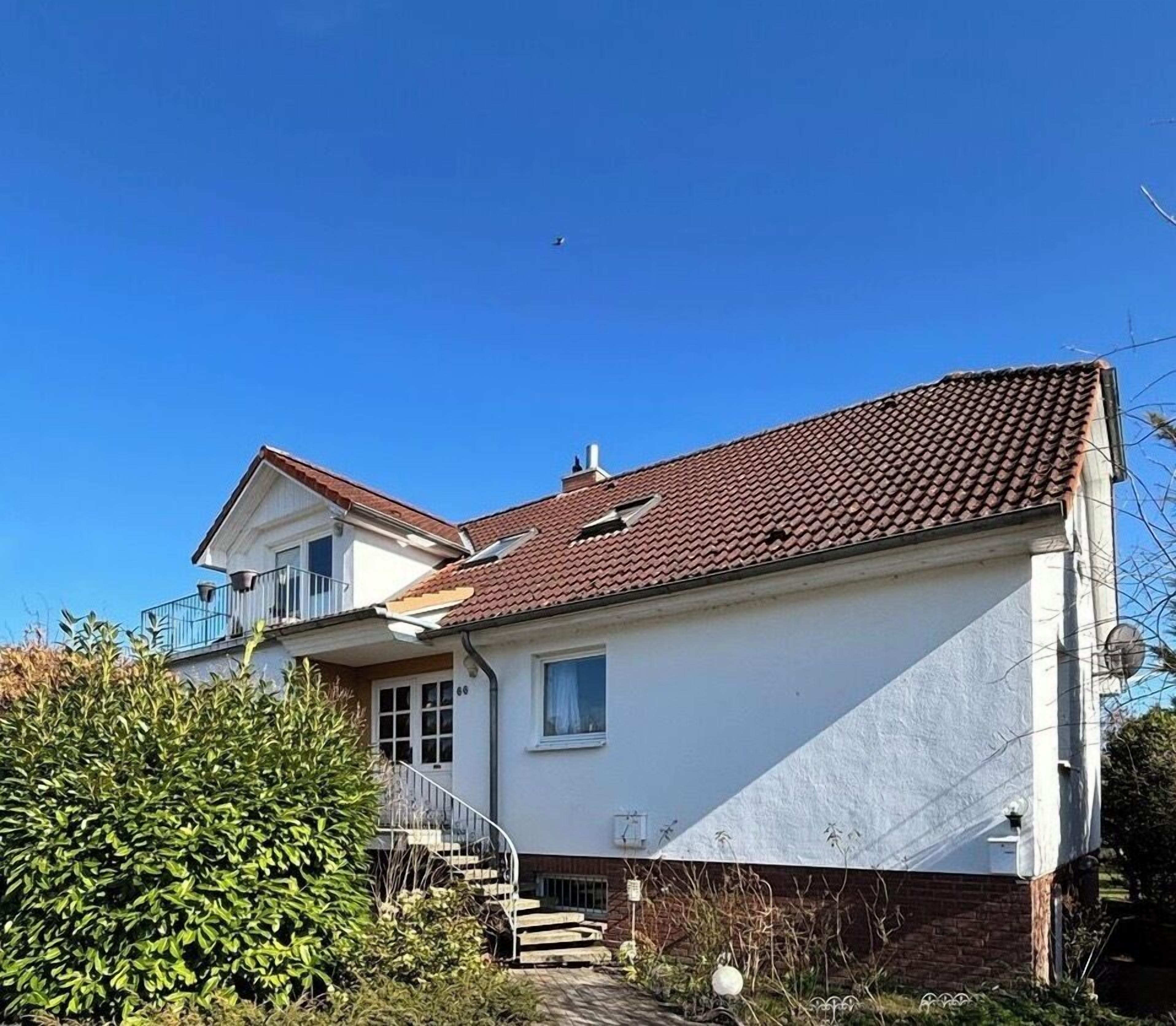 A two-story house with a red-tiled roof, a balcony, and a small garden area.