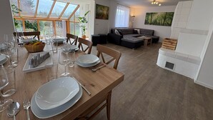 Een moderne woonkamer met een eethoek, grote ramen en een open haard.