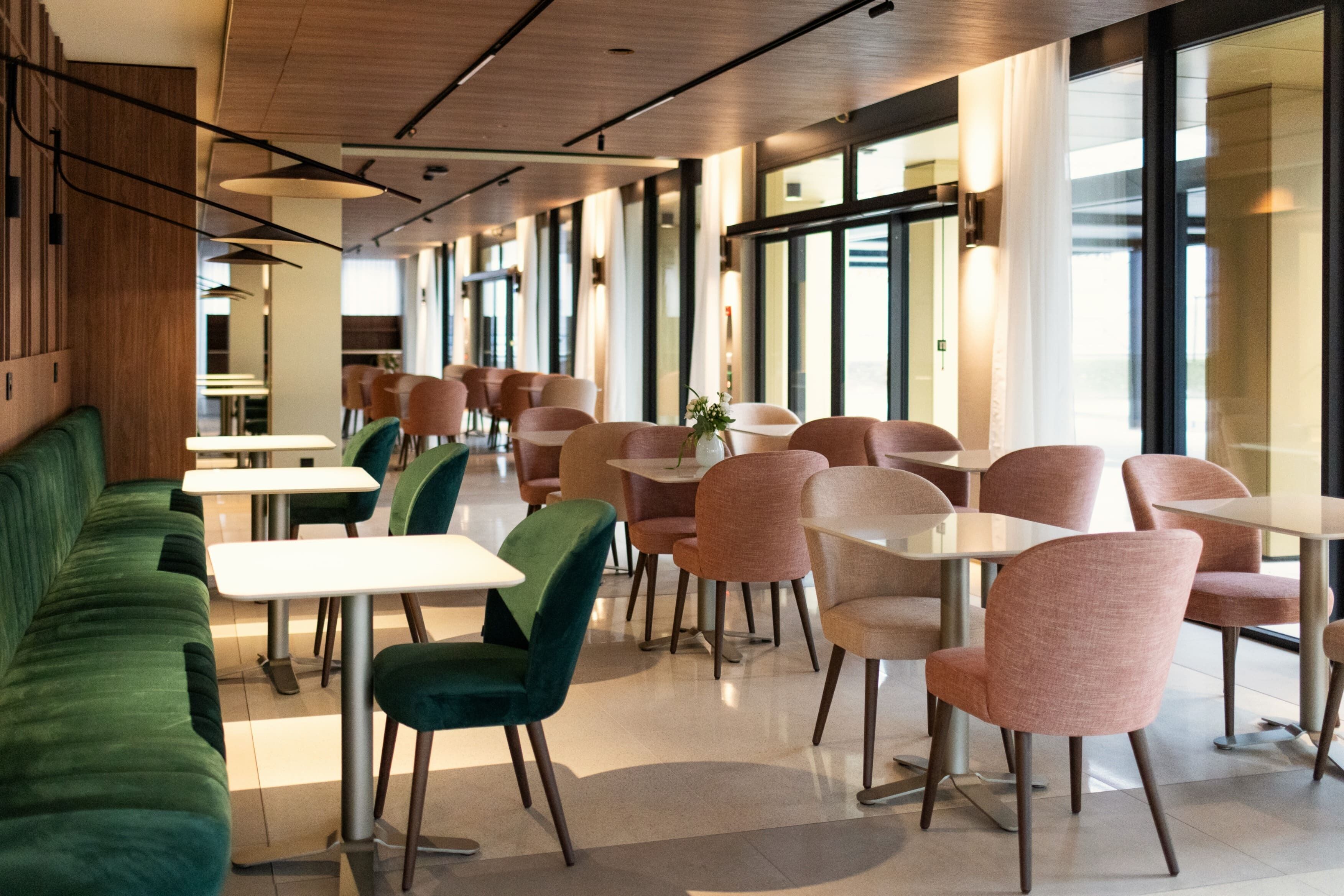 Un comedor moderno con sofás verdes, sillas rosas y mesas blancas.