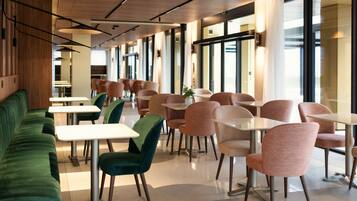 Un comedor moderno con sofás verdes, sillas rosas y mesas blancas.