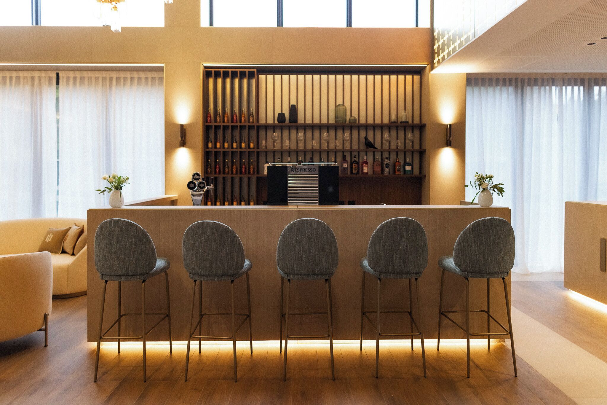 Un espace bar moderne avec un comptoir, des tabourets de bar et une présentation de bouteilles et de verres.